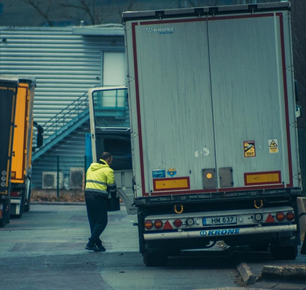 pexels-photo-11114134 A truck driver in high-visibility gear unloading cargo at an industrial facility.