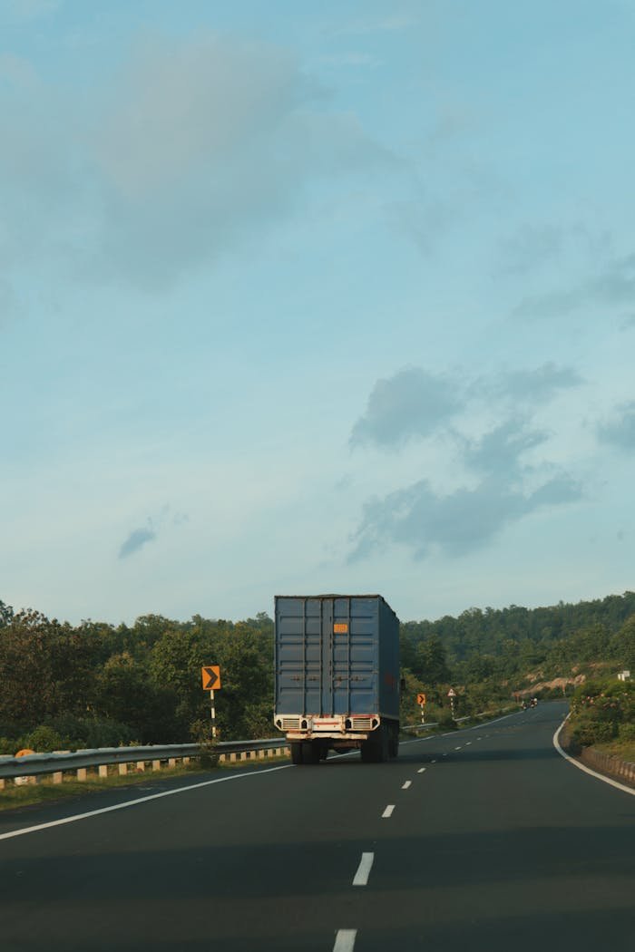 A cargo truck driving on an open highway surrounded by nature. Ample copy space available.